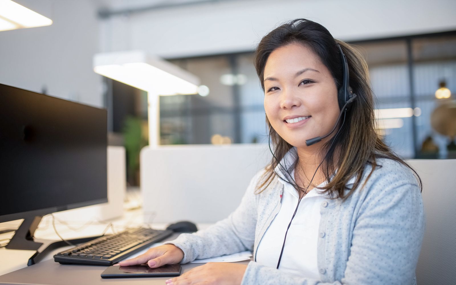 Smiling call center agent wearing a headset while working at her desk in a modern office setting.