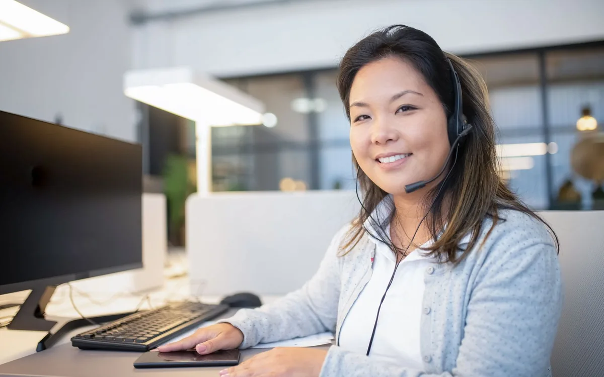 Smiling call center agent wearing a headset while working at her desk in a modern office setting.