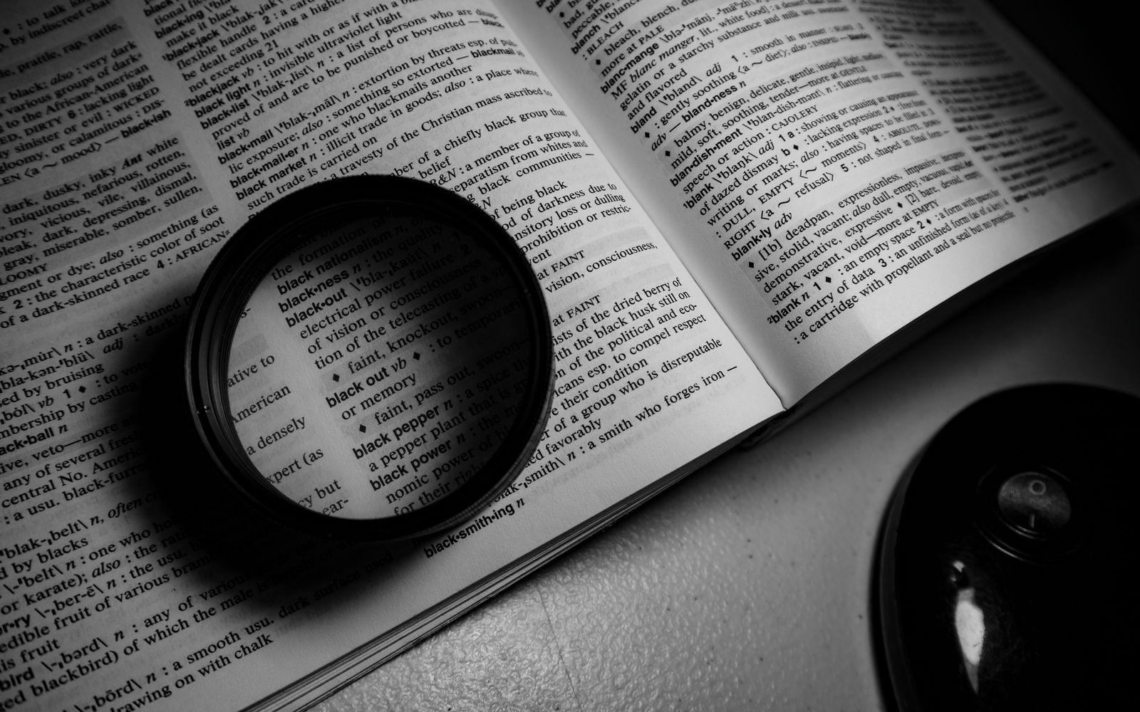 A monochrome image of a lens on an open dictionary page, highlighting words.