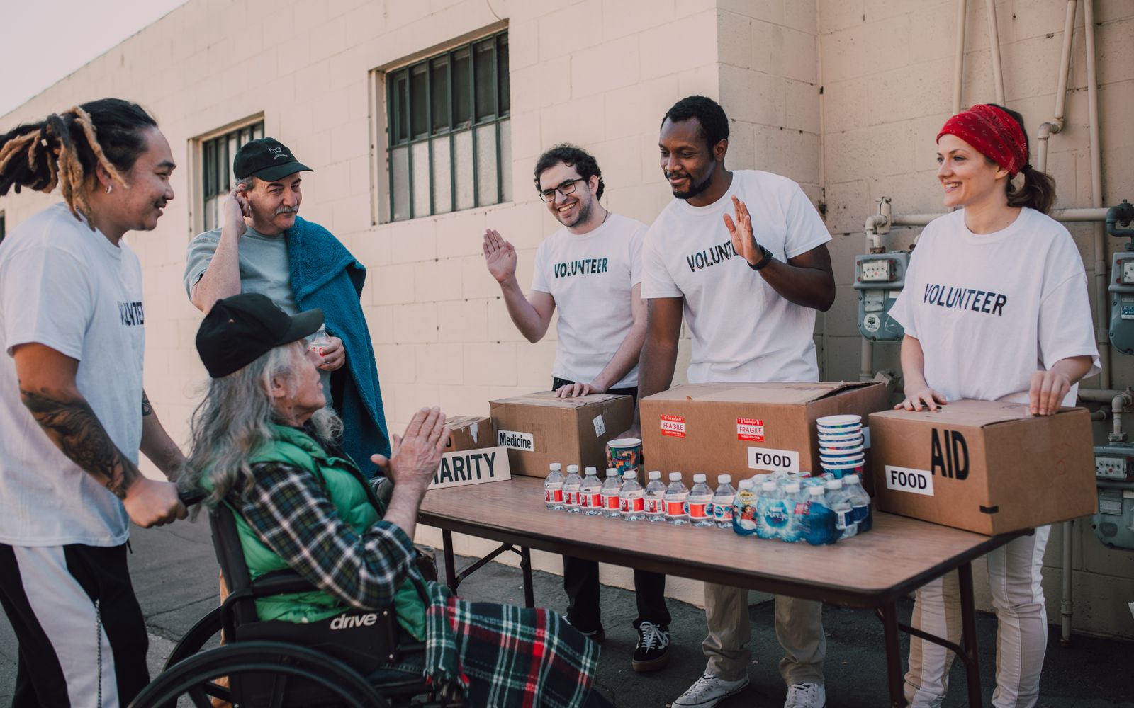 Group of volunteers providing food and aid to a person in wheelchair outdoors.