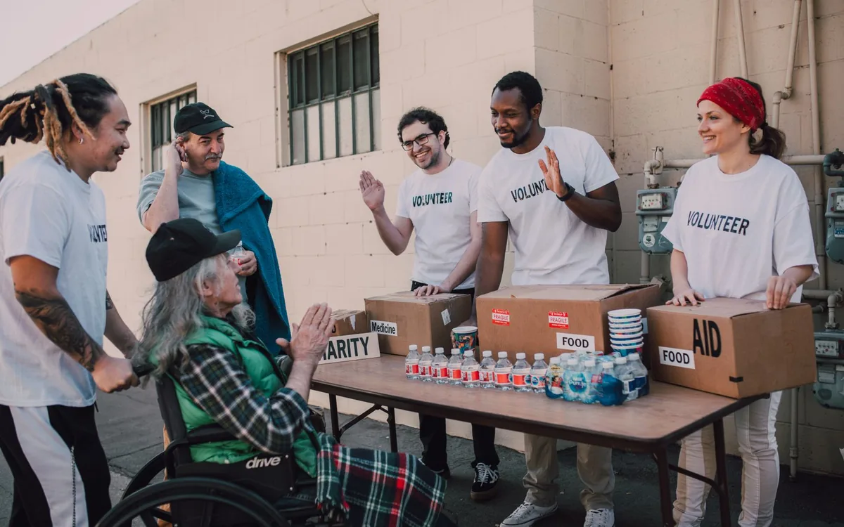Group of volunteers providing food and aid to a person in wheelchair outdoors.