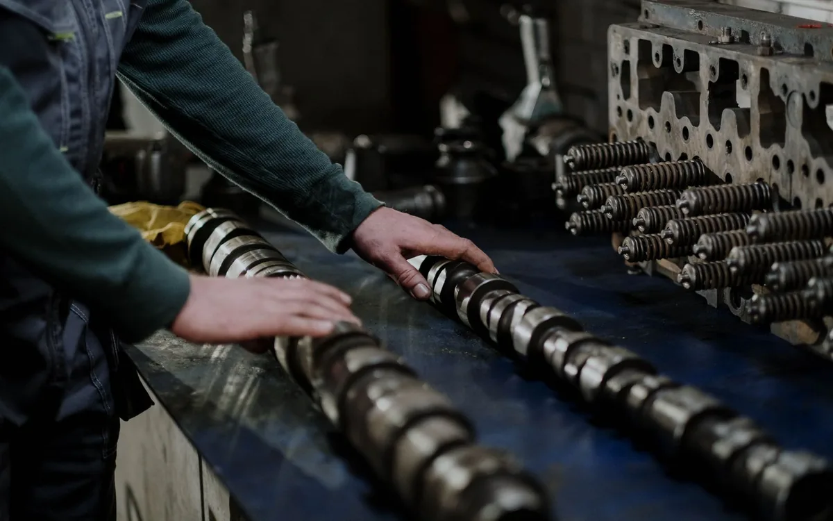 Worker handling camshafts and cylinder head in a mechanic workshop.
