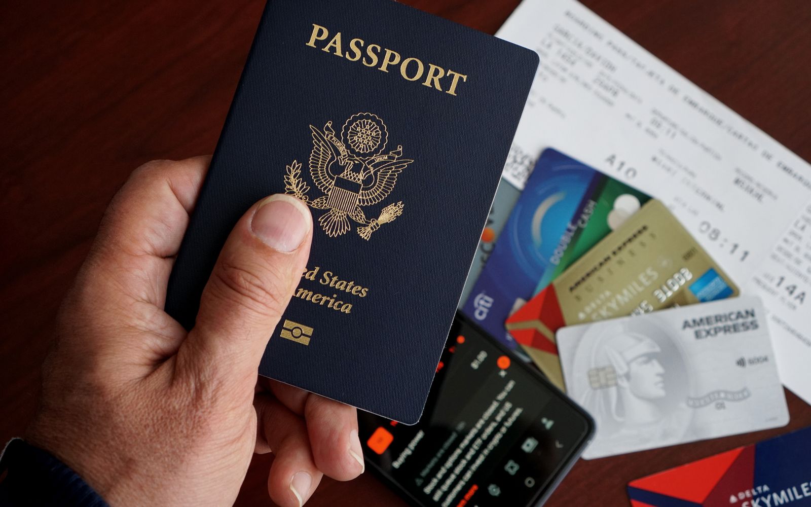A close-up of a US passport with credit cards, tickets, and a mobile phone on a table.